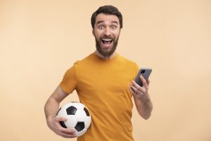 portrait-excited-young-man-looking-his-smartphone-holding-ball