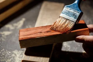 Imagem de uma pessoa aplicando resina epóxi em uma madeira, ideal para quem procura onde comprar resina epóxi para madeira. A resina proporciona acabamento e proteção.