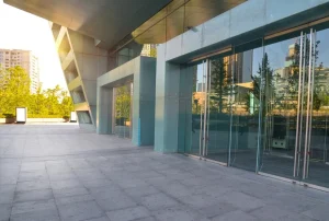 Fachada comercial atrativa com vidro e detalhes modernos, ideal para atrair clientes. O ambiente é iluminado e espaçoso, com vegetação ao fundo.