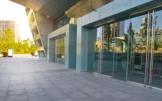Fachada comercial atrativa com vidro e detalhes modernos, ideal para atrair clientes. O ambiente é iluminado e espaçoso, com vegetação ao fundo.