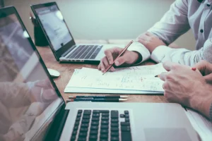 Reunião de negócios focada em finanças pessoais e empresariais, com notebooks, planilhas e uma pessoa anotando estratégias financeiras.
