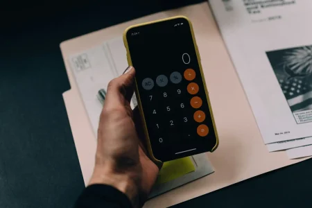 Pessoa controlando gastos financeiros utilizando uma planilha gratuita em um celular, com detalhes de calculadora na tela, ao lado de documentos e papéis.