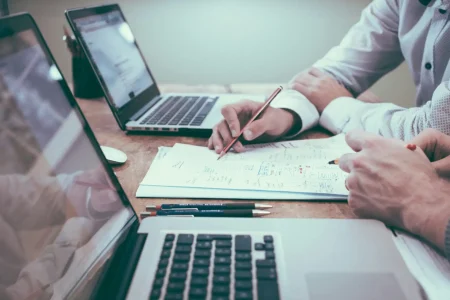 Pessoa analisando documentos e usando laptops, relacionados às indústrias de base, que são essenciais para o desenvolvimento econômico devido ao impacto na produção de bens essenciais.