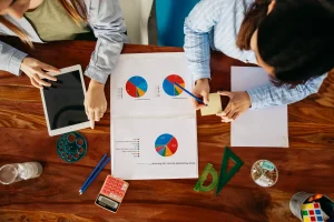 Reunião de profissionais analisando gráficos de tecnologia e orçamento empresarial, com tablet, calculadora e materiais de escritório sobre uma mesa de madeira, ilustrando dicas de como investir em tecnologia sem comprometer o orçamento da empresa.