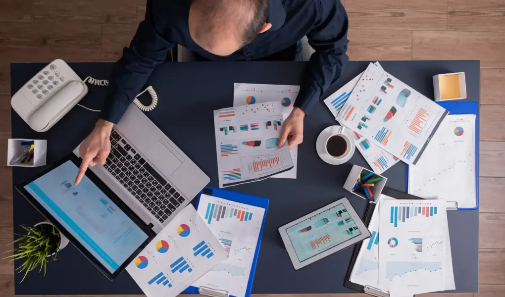 Imagem de um escritório com documentos, tablet, computador portátil e telefone, focada em gestão financeira de pequenas indústrias, abordando contas a pagar e receber.