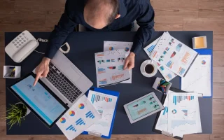 Imagem de um escritório com documentos, tablet, computador portátil e telefone, focada em gestão financeira de pequenas indústrias, abordando contas a pagar e receber.