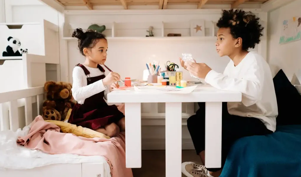 Crianças criando uma atividade de arte em casa, ideal para DIY: quadros, vasos e luminárias feitas em casa, em um ambiente aconchegante com brinquedos ao redor.