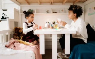 Crianças criando uma atividade de arte em casa, ideal para DIY: quadros, vasos e luminárias feitas em casa, em um ambiente aconchegante com brinquedos ao redor.