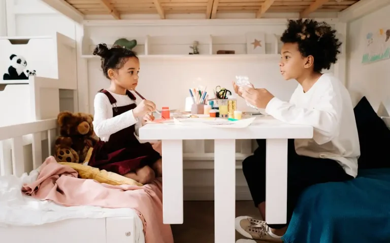 Crianças criando uma atividade de arte em casa, ideal para DIY: quadros, vasos e luminárias feitas em casa, em um ambiente aconchegante com brinquedos ao redor.