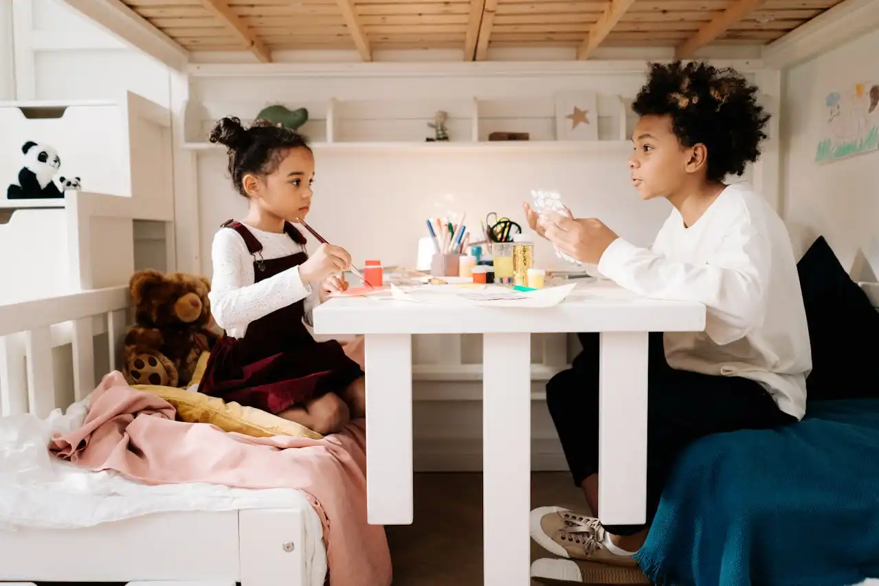 Crianças criando uma atividade de arte em casa, ideal para DIY: quadros, vasos e luminárias feitas em casa, em um ambiente aconchegante com brinquedos ao redor.