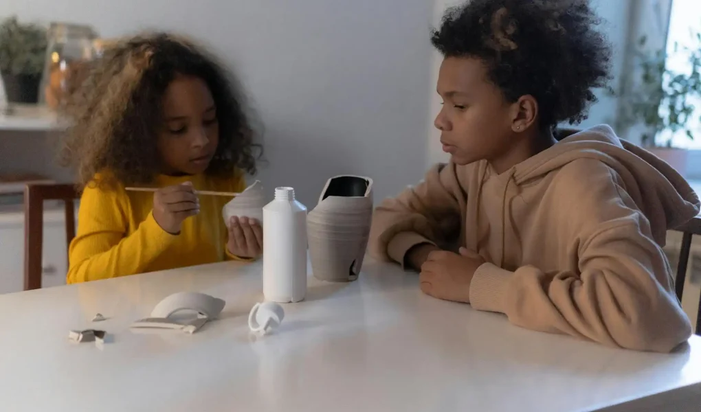 Crianças criando pinturas em objetos de porcelana como parte de uma atividade de artesanato, ilustrando criatividade na transformação de móveis antigos com pintura.