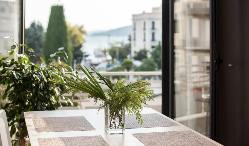Imagem de uma varanda bem decorada com uma mesa de jantar, vaso de plantas verdes e vista para a cidade, ideal para dicas de aproveitamento de varandas e cantinhos da casa.