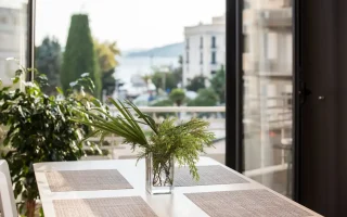 Imagem de uma varanda bem decorada com uma mesa de jantar, vaso de plantas verdes e vista para a cidade, ideal para dicas de aproveitamento de varandas e cantinhos da casa.